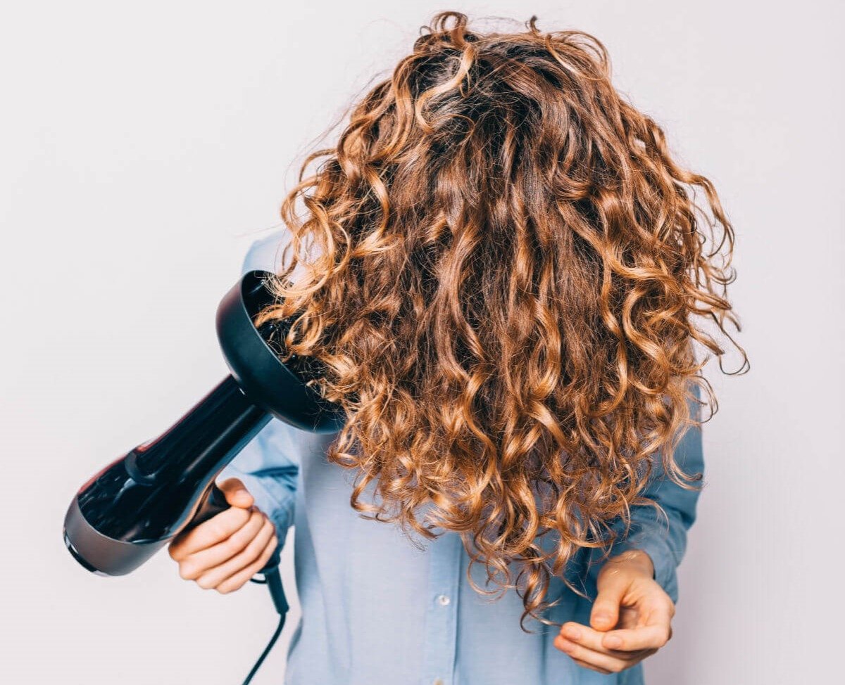 Mujer secando el pelo rizado con un difusor
