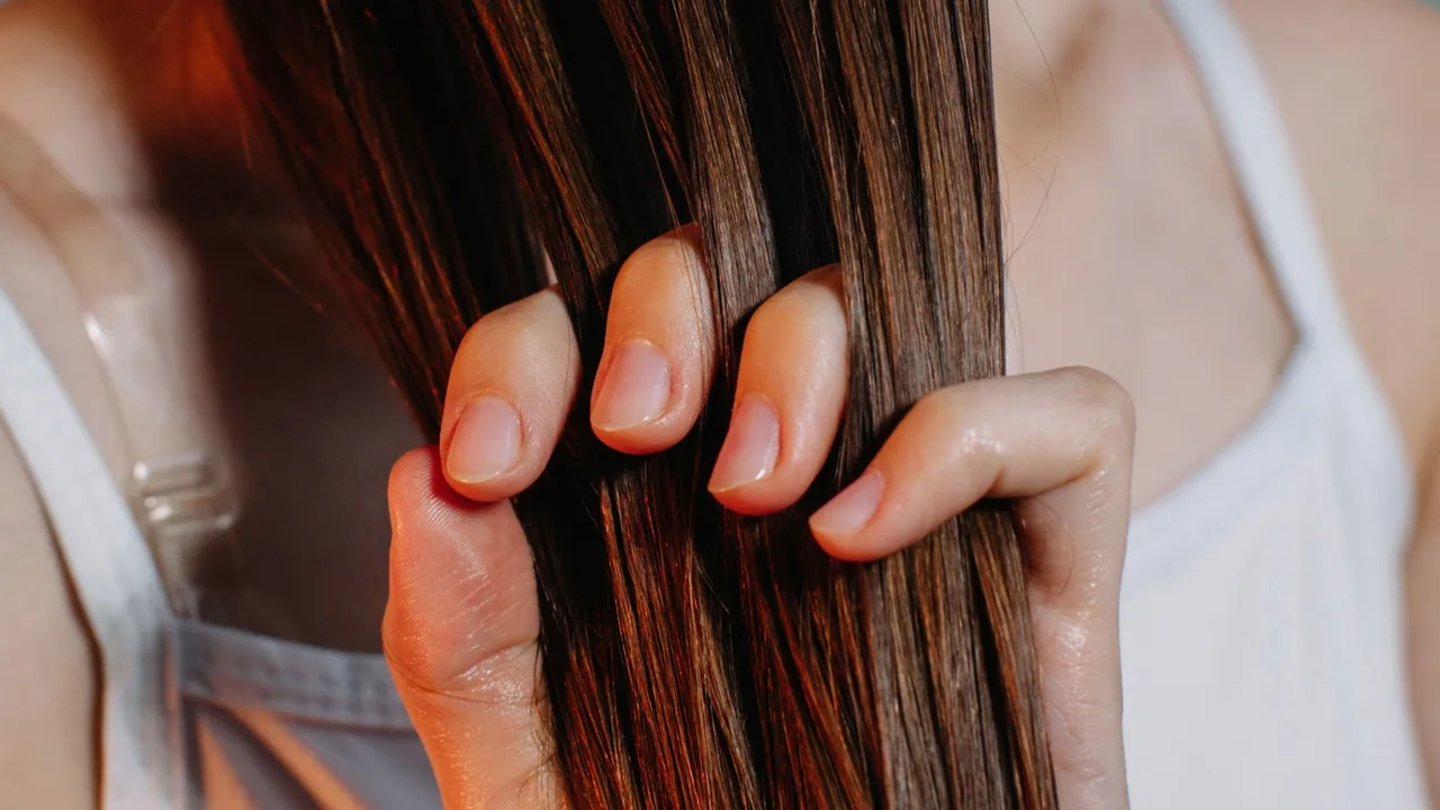 Mujer peinando su cabello con las manos usando aceite de almendras