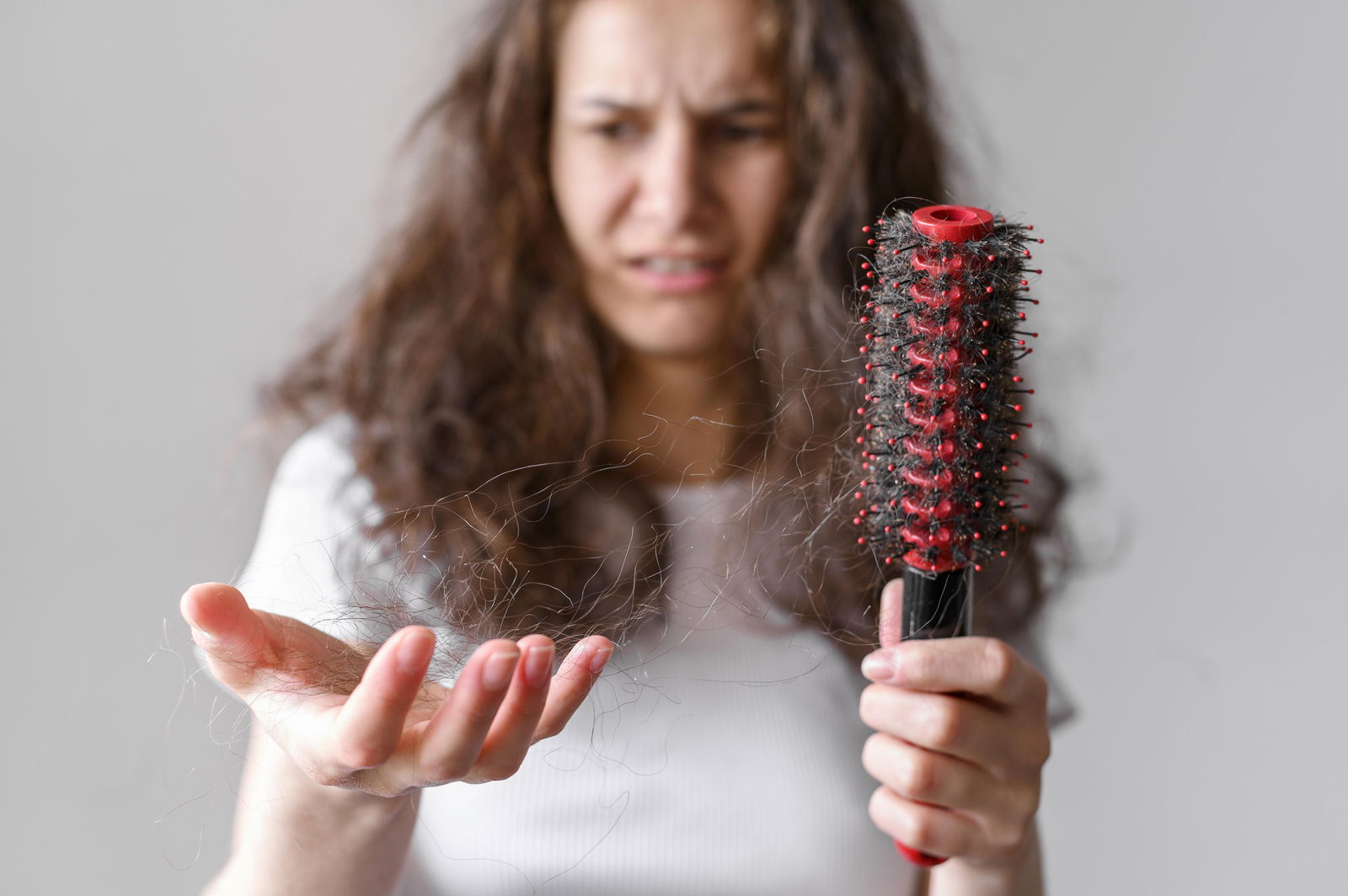 Mujer observando pelos sueltos tras cepillarse, signo de cabello debilitado y frágil.